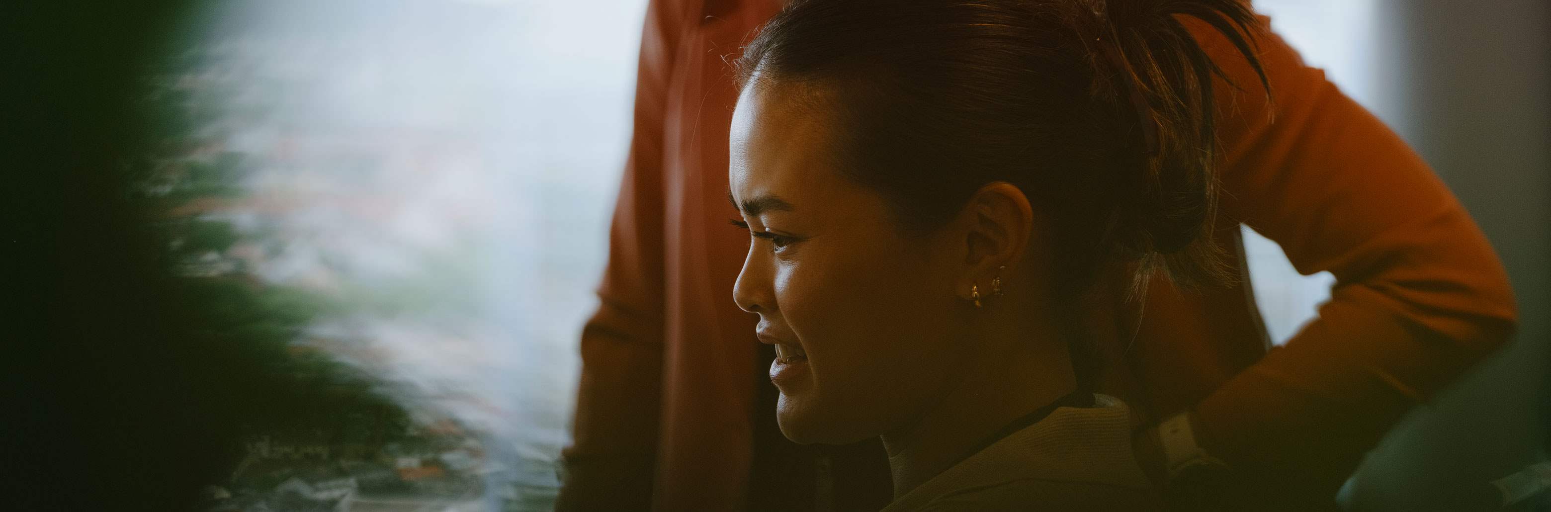 Kvinne med halvlangt mørkt hår som smiler inne i et møterom med hvit tavle.