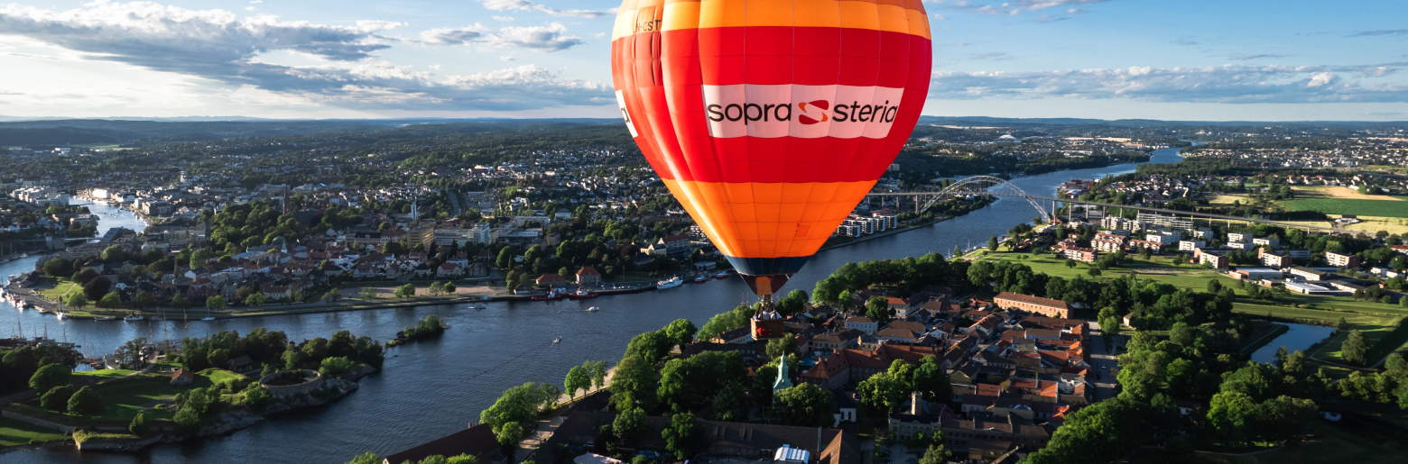 Oransje luftballong med Sopra Steria-logo svever over bylandskap